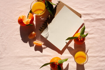 Two glasses of orange juice and a white sheet mockup on a notepad on a pink background. Contrasting shadows. View from above