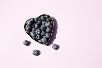 Blueberries in a heart-shaped plate on a pink background with contrasting shadows. View from above