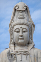 Giant white Guan Yin statue at Guanyin Bodhisattva Pavilion in Kanchanaburi, Thailand. Beautiful Chinese goddess sculpture against blue sky, famous religious landmark for tourism.