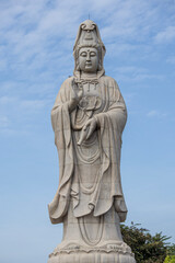 Fototapeta premium Giant white Guan Yin statue at Guanyin Bodhisattva Pavilion in Kanchanaburi, Thailand. Beautiful Chinese goddess sculpture against blue sky, famous religious landmark for tourism.