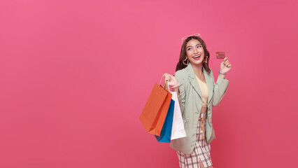 Happy pretty Asian woman carrying colorful shopping bags with credit card isolated on pink studio...