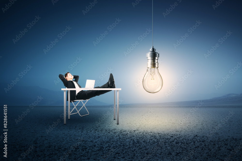 Poster A man relaxing at a desk in a vast space with an illuminated bulb overhead, embodying a concept of inspiration
