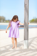 Happy little blonde girl in lilac summer dress playing and has fun on a white sandy beach near the ocean in summer. Children's holidays. Earth Day. Children's Day. Vacation concept. Space for text