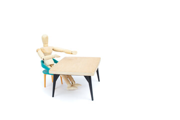 Fototapeta premium Wooden mannequin sitting on a chair at a empty wooden table isolated on white background, inviting gesture Hiring interview sign template concept
