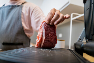Chef at the kitchen preparing beef steaks on the home electric grill