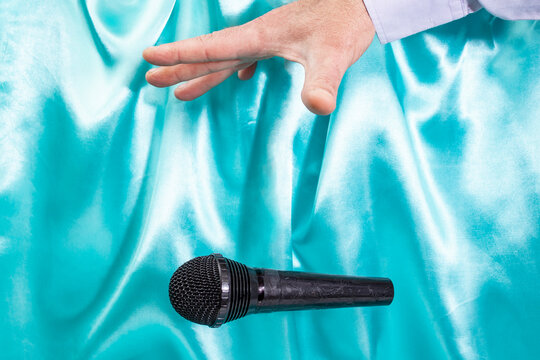 Caucasian male's hand dropping the mic, stretched hand and a microphone soft focus close up on turquoise satin background
