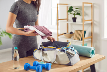 Close up shot of a woman packing a sport bag with equipment and sportswear on table at home. Preparing for a active gym workout, planning fitness and gymnastics or aerobics activities.