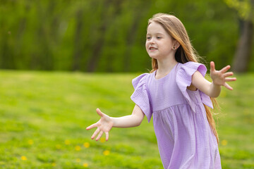 Cute happy laughing little girl having fun on the grass in the meadow in the park, playing on a warm sunny weekend. lifestyle. space for text. High quality photo