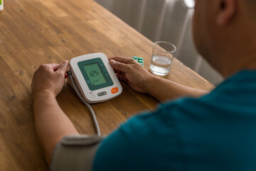 Seniory man checks blood pressure with monitor on upper arm in room 