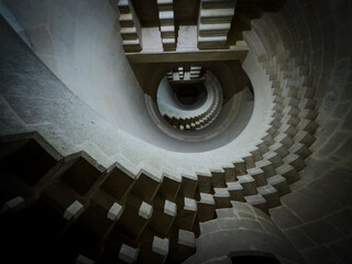 Circular stairs of old fortress twist down in moody ambiance