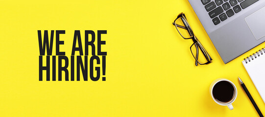 We are hiring. Desk with laptop, eye glasses, flower, pen and a cup of coffee. Still life,...