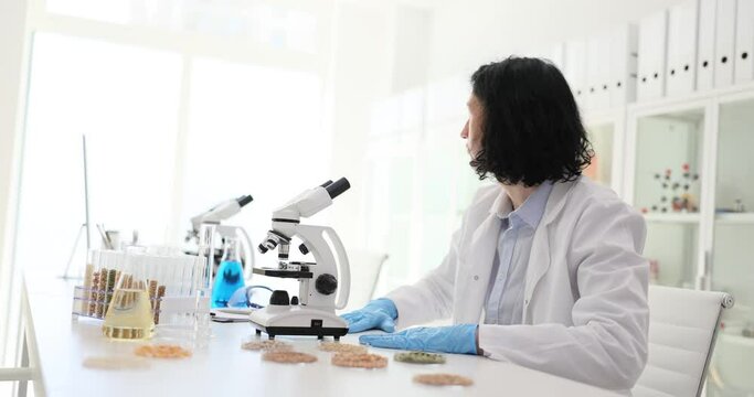 Nutrition expert testing food products in lab. Scientist chemist looks into microscope with test tubes with grains in laboratory