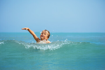 A cute blond young boy enjoying warm sea waves splashing around