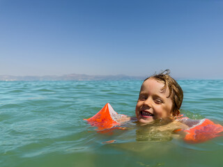 Young swimmer boy enjoys the ocean in bright orange arm bands