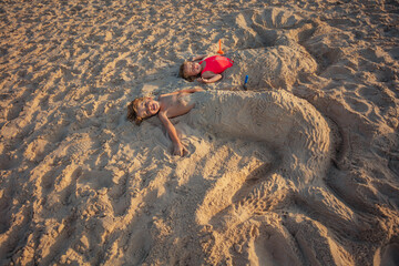 Boy and girl enjoy sandy mermaid sculpture play at sunset beach