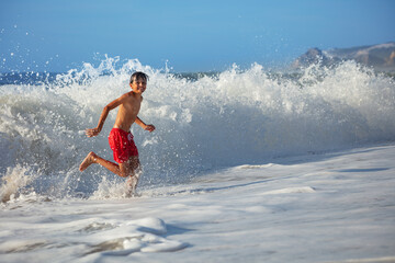 Young boy running along shoreline with ocean waves crash around