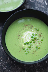 Black bowl with cream-soup made of green peas, vertical shot on a dark-brown granite background, middle closeup