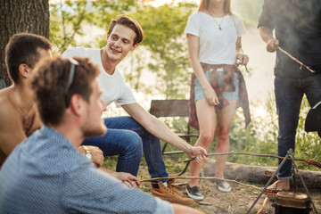handsome smiling man in T-shirt and jeans is sitting with stick among friends. close up cropped...