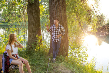 a couple smiling happily and looking at each other. beautiful landscape on the background of the photo. attractive man is leaning on the tree and talking with nice girl who is sitting on the chair