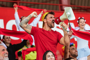 Sport fans are cheering for their team at the stadium on the match. The cheer leader uses a megaphone