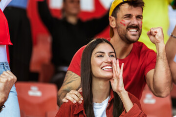 Sport fans are cheering for their team at the stadium on the match in red colors.