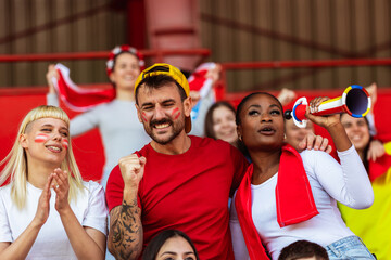 Sport fans are cheering for their team at the stadium on the match in red colors.