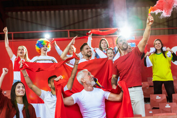 Fototapeta premium Sport fans lit torches in the stadium at the game. Red colors, flags, stadium.