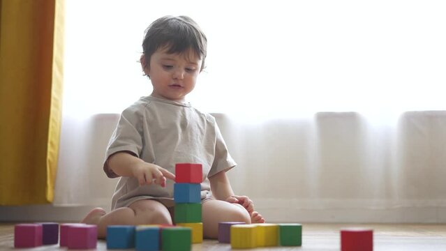 Cinematic shot. happy child home in room with cubes. child dream. child assembles tower from cubes in room at home on floor. happy family concept. child with cubes in room at home. games at home.