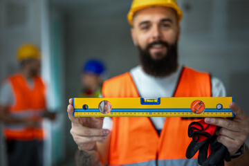 Close up of spirit level. Construction site manager standing  wearing safety vest and helmet.