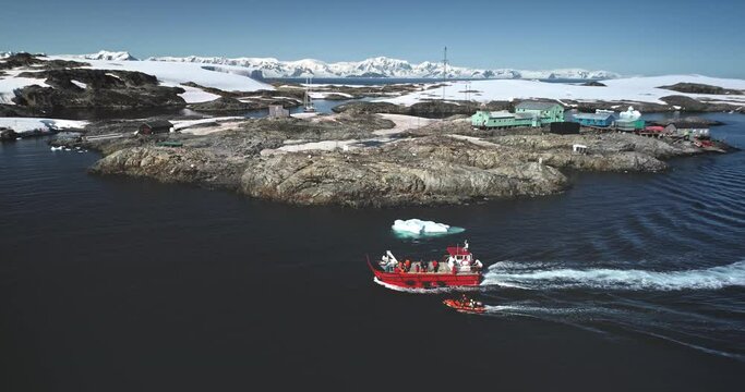 People travel to Antarctica. Explore South Pole. Tourists on red boat zodiac sailing polar ocean enjoy wild nature ocean landscape with snow covered mountains. Tourism expeditions. Aerial drone shot