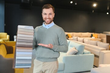 Handsome stylish boy with beard sitting, holding palette, looking, touching. Concept of furniture buying