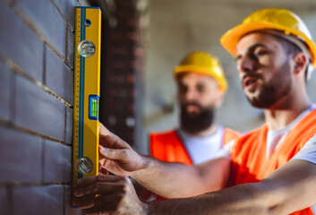 Construction worker working with spirit level on a construction site. Other workers helping.