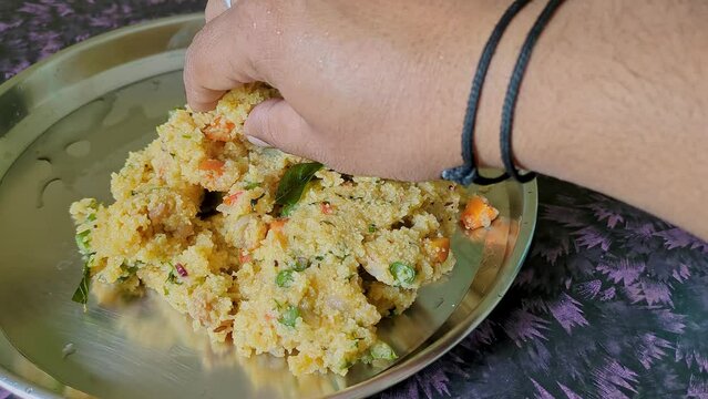 Close-up of a male hand eating homemade Indian breakfast broken wheat porridge or upma