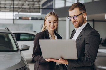 Portrait of two workers with laptop inside car showroom