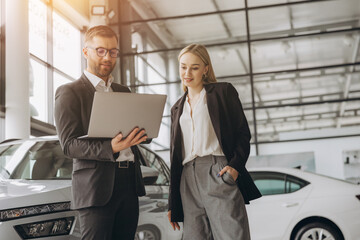 A male salesman showing something on a laptop to a female client buying a car inside a car dealership