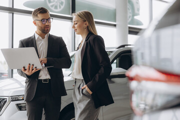 A male salesman showing something on a laptop to a female client buying a car inside a car...