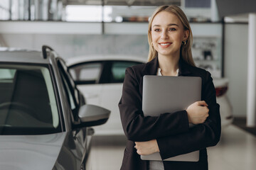Pensive stylish businesswoman manager in suit holding laptop computer, standing near car at car...