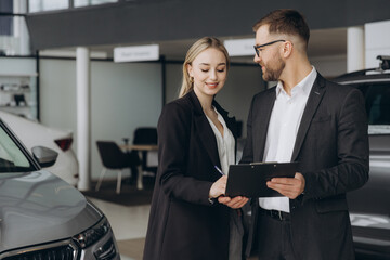 Car Sales Manager Showing Auto To Caucasian Lady Buyer Standing In Luxury Automobile Dealership...