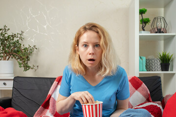 Shocking movie content, woman watching TV in surprise, eating snack on sofa, thrilling cinema...