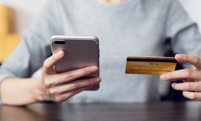 Woman hand holding a credit card and using smartphone to pay online. The concept of online shopping and payment.