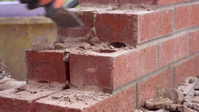 Builder breaking brick wall with chisel and hammer