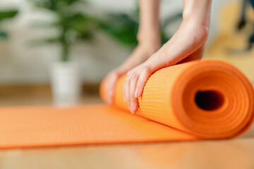Woman rolling orange fitness yoga mat.