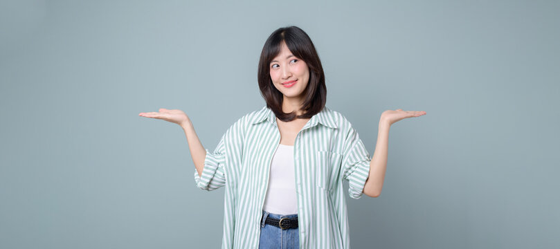 Lifestyle, people emotions and casual concept. Cute smiling asian woman enterpriser introduce two products, hold hands sideways as if demonstrating products on palms, standing pastel green background