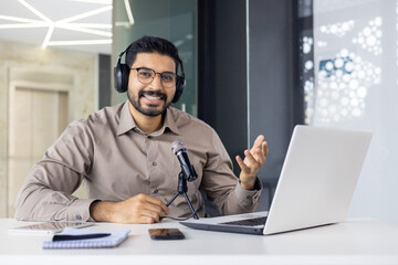 A man is podcasting at a desk with a laptop, microphone, and headphones, showcasing modern audio...