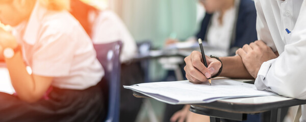 Exam at school with student's taking educational admission test in class, thinking hard, writing answer in university classroom, education and world literacy day concept