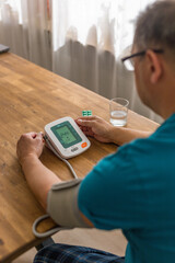 Seniory man checks blood pressure with monitor on upper arm in room 