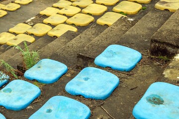 Old, blue plastic stadium seats with bright yellow seats in the background going up a level with...