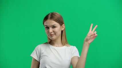 A woman, close-up, on a green background, shows a victory sign