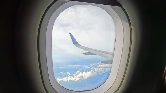 View of airplane wings in clouds through porthole. Blue sky background. Beautiful clouds and airplane wings from the window with beautiful blue sky
