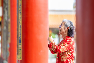 Asian senior woman in red cheongsam qipao dress is making a wish to ancestral god inside Chinese...